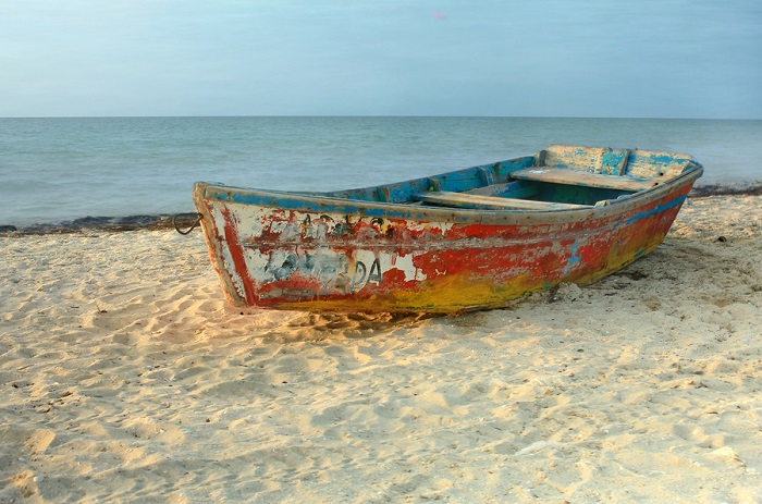 Solo rowboat with peeling paint resting on sandy beach