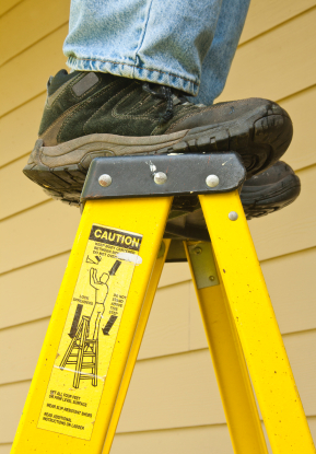 man standing on the top step of a ladder with caution sticker showing danger
